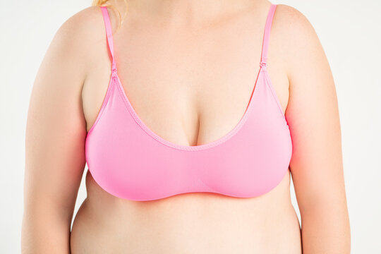 Large natural saggy breasts with asymmetry after breastfeeding in a pink top bra close-up, big boobs on gray background, augmentation and plastic surgery concept