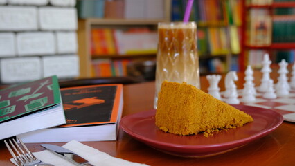 a slice of cake, a glass of cold coffee, book and chess board