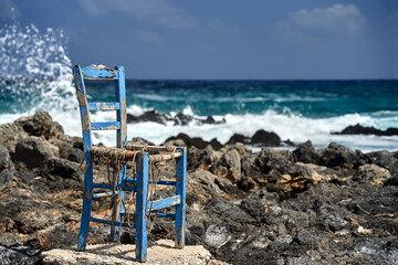 An old, worn-out chair on the rocky coast of the Mediterranean Sea on the island of Crete