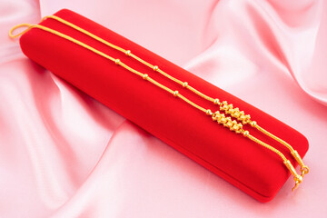 Gold necklace on a red velvet box on a pink fabric background.