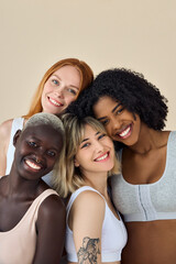 Happy cool fashion gen z girls in underwear looking at camera, beauty portrait. Four smiling diverse young women, multicultural ladies models bonding isolated on beige background. Vertical