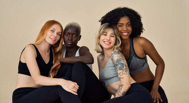 Happy diverse fit sporty active young women, four multiracial beauty models wearing sportswear sitting at beige background advertising yoga group gym trainings, team fitness pilates workout. Portrait.