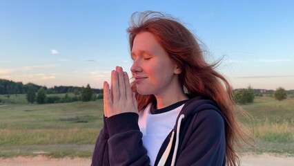 young cute woman dreaming and praying outdoors at sunset or sunrise in the park