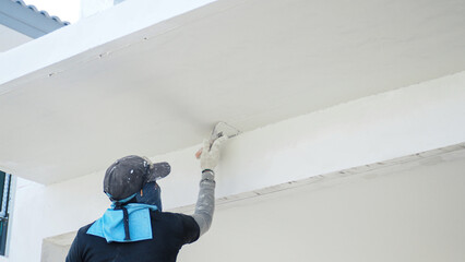 A painter is covering a reinforced concrete awning in front of a house to create a smooth,...