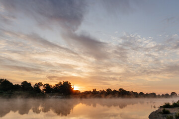 Beautiful landscape with a river and reflection, thick fog at dawn. Lake in the early morning in thick fog