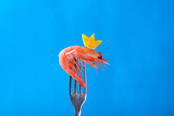 Boiled shrimp with a lemon crown on fork against blue background. Copy space. Conceptual funny composition - 658689062