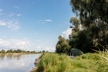 Beautiful summer landscape by the river ion the sunny summer day. The tent stands among green grass...