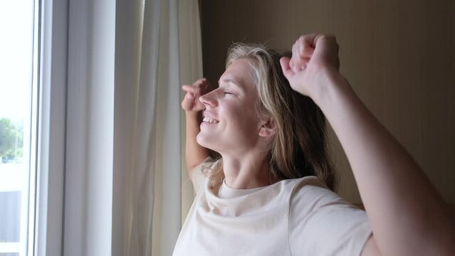 closeup of woman waking up and stretching in the morning in hotel room by the window