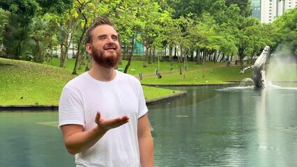Positive young man smiling during the rain in the park. Cheerful male enjoying the rain outdoors. Guy looking up and catching the rain drop with hands. Breath deep and relax in Malaysia 