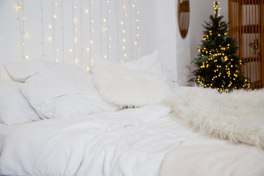 Christmas decorated bedroom interior with comfortable bed, Christmas fir tree and gift boxes on floor, copy space. Cozy home moment. Happy New Year. christmas garland lights at home