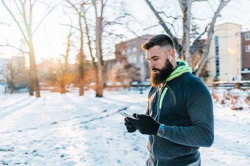 Handsome middle age man with a beard running and exercising outside on extremely cold and snowy day. Sport and fitness motivation theme. He using smart phone to track his activity data.