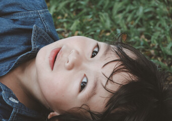 A young boy lies sprawled on the grass, eyes wide open, capturing a captivating and serene moment.