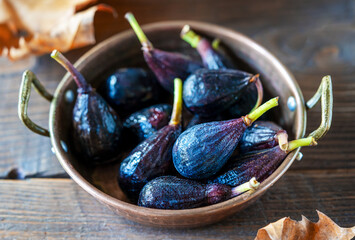 Raw figs in a coper bowl over wooden background with autumn leaves