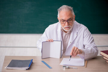 Old male teacher in front of green board