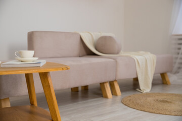 Fototapeta na wymiar Work from home, renting apartment, buying. beige sofa with pillows, table with cup of hot drink, shelves in living room interior.Concept of morning cup of coffee, good start to the day, a cozy home.