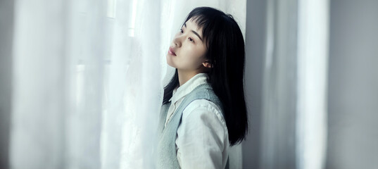 An autistic Asian girl leaning against the window - obrazy, fototapety, plakaty