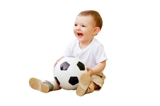 Happy toddler baby boy is playing walking behind a soccer ball, first steps, isolated on a white background. Smiling child in white clothes walks with a ball, age one year