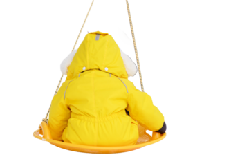 Toddler baby rides in the snow on icesled, a winter playground, isolated on white background. Mother woman sledding baby boy in yellow snowsuit. Kid age one year eight months