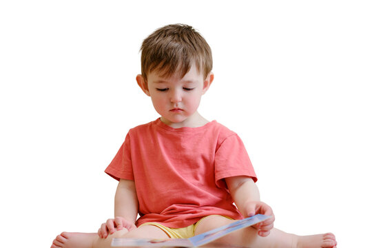 The cute baby is playing with the colorful picture book, flipping through the pages and touching the pictures, isolated on white background. The little child is lost in thought as he reads book
