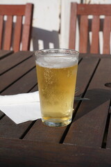 half pint of cold beer on wooden garden table. refreshing cool glass of larger beer.