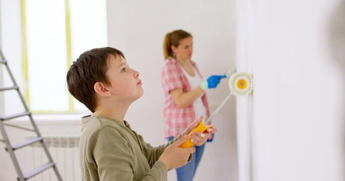 Happy family mother and son paint the wall with paint using roller and brush