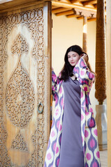 Beautiful fashion model, girl in traditional Uzbekistan fashion dress with ikat pattern open door. Tashkent, Uzbekistan