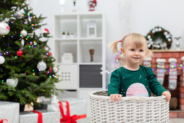 A young child with blonde hair plays by the Christmas tree