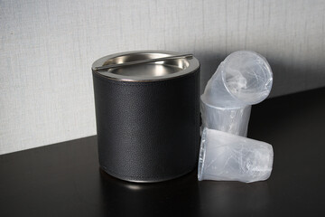 Leather ice bucket with disorganized wrapped plastic cups on table