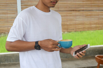 Close up of Asian man holding a cup of coffee and mobile phone. Technology and morning routine concept