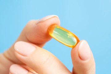Close-up of female hand holding omega 3 fish oil capsule. Vitamin pill or supplement on blue...