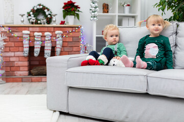 Brother and sister sit together on a couch by a brick fireplace