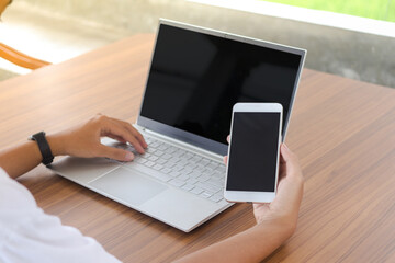 Close up of businessman hand touching blank screen of mobile phone with laptop beside on the table....