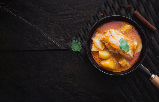 Top view of massaman curry with chicken and potatoes in pan on wooden background. Thai Food