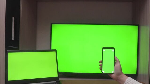 Laptop, HDTV and a woman's hand holding up a mobile phone with green screens, with copy space. Chroma key screen concept for product presentation, online orders and layout