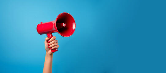 Woman's hand with red nails holding megaphone loudspeaker on solid plain blue studio background. Important announcement news significant messages sale discount concept. Empty place for text copy paste