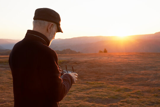 A man takes a picture of a sunrise in the mountains with a quadcopter. He is holding the remote control of the drone. Copy space.