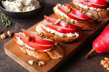 Crostini appetizers with red pears, whipped feta cheese and walnuts. Close up table scene against a...