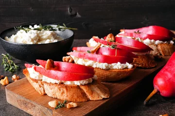 Foto op Canvas Crostini appetizers with red pears, whipped feta cheese and walnuts. Close up table scene against a dark wood background. Party food concept. © Jenifoto