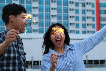 carefree asian young couple holding sparklers celebrate new year with city building background,...