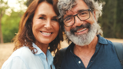 Close up, smiling older married couple looking at the camera while standing in the park hugging...