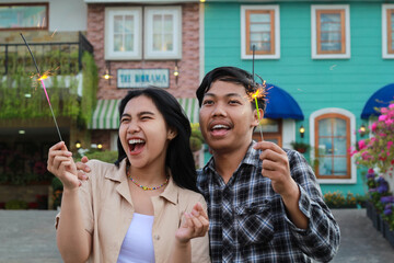 exited asian young couple holding sparkler and shouting in the yard of vintage wooden house...