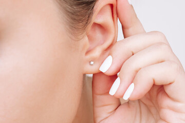 Ear piercing. Cropped shot of a young woman wearing elegant stud earrings. Jewelry with gemstones,...
