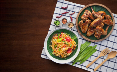 Top view of papaya salad with grilled chicken wings on wooden background. Famous local Thai street food
