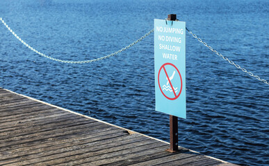 Sign no jumping, no diving from wooden pier, shallow water. Dangerous warning sign.