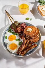 full american classic breakfast with fried eggs, sausages, fried, bacon, pancakes and espresso and orange juice close up top view. recipe book concept or food photo for print