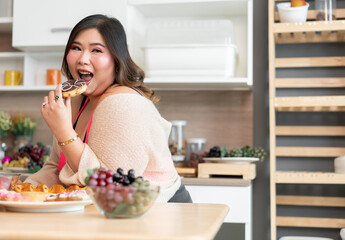 Copy space Happy Asia plus size woman eating donut in kitchen at home