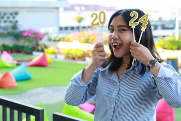 excited young woman asian looking at camera and standing on railing of house yard to celebrate new year eve with holding 2024 number candle, outdoor - obrazy, fototapety, plakaty
