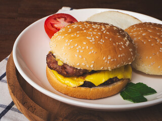 Homemade cheese burger in white plate on wooden table.