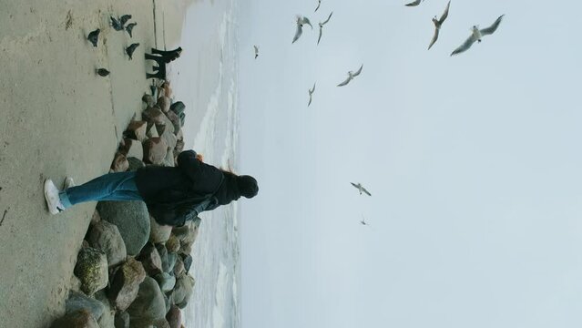 The girl is happy feeding seagulls with bread on the seashore.