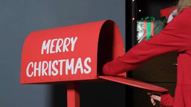 Close-up of hand of little girl putting letter to Santa into a mailbox indoors. Winter holidays and New Year concept